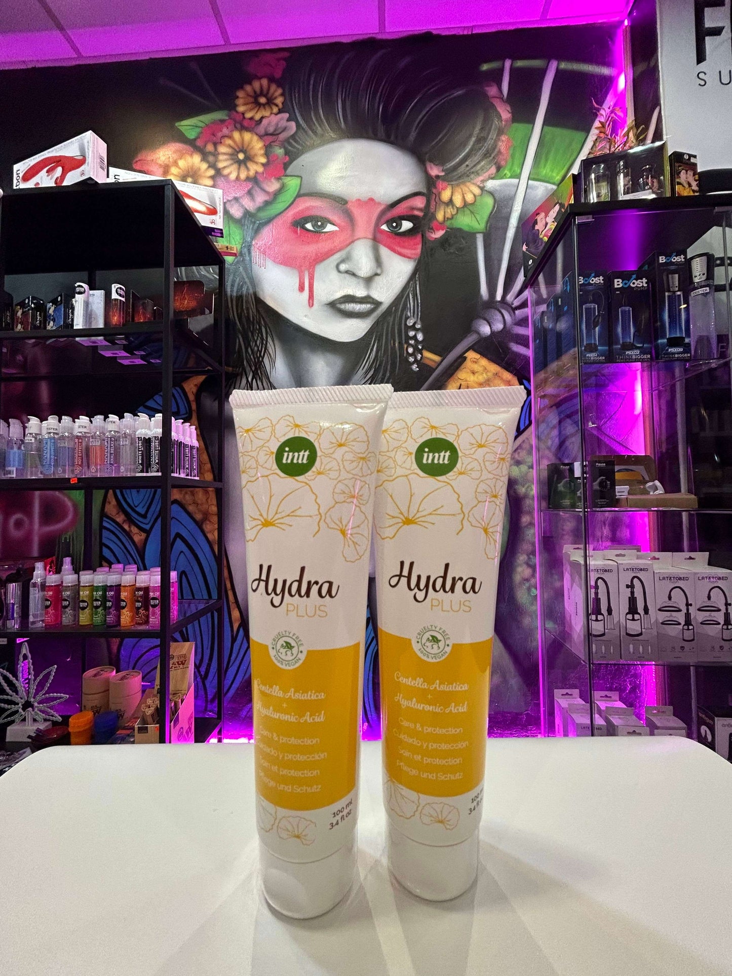 Tubos de lubricante ácido hialurónico Hydra Plus frente a un mural artístico colorido.