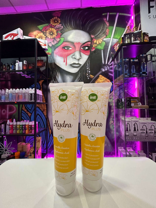Tubos de lubricante ácido hialurónico Hydra Plus frente a un mural artístico colorido.